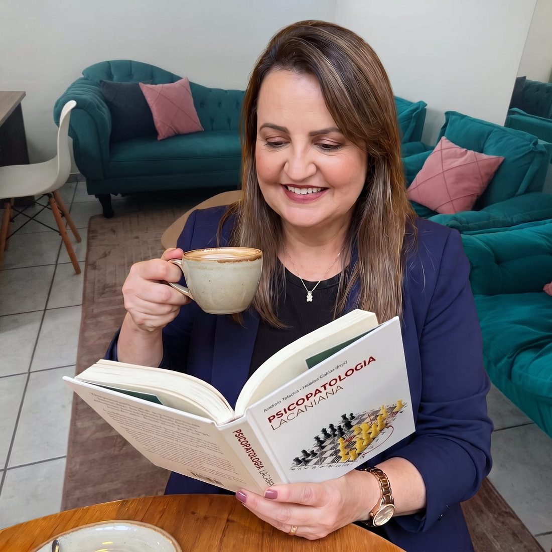 Renata Madrazo sorrindo com uma xícara de café e um livro de psicopatologia lacaniana